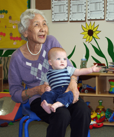 Elderly women sitting on a chair, smiling with a baby on her lap