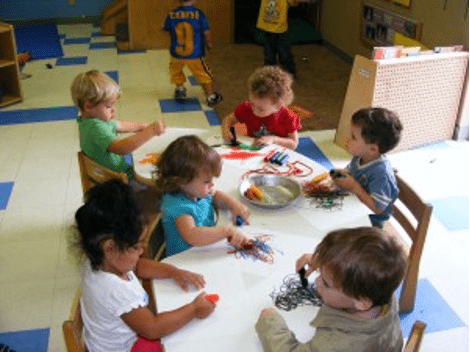 Six small children sitting together at a table playing and talking to one another
