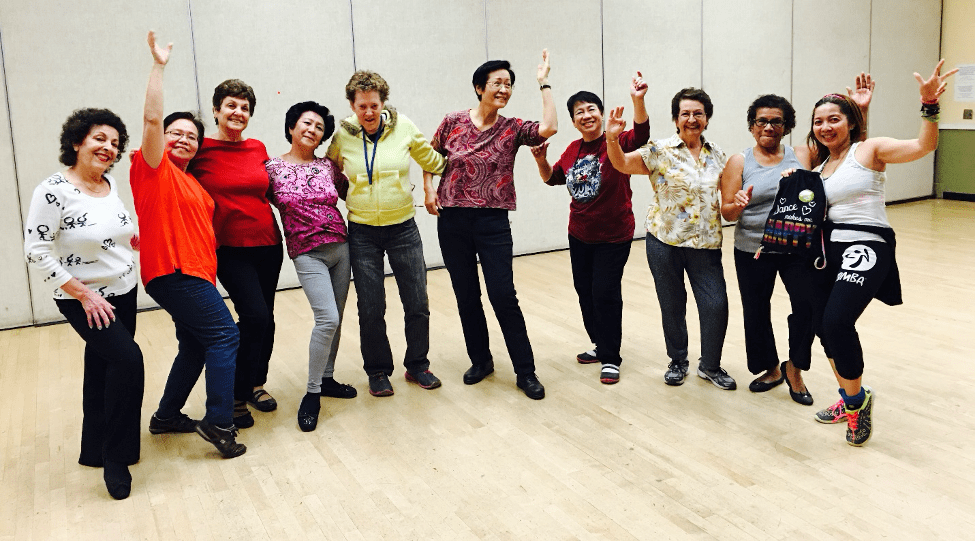 Several seniors standing together with smiles and their hands in the air. They are in a dance studio