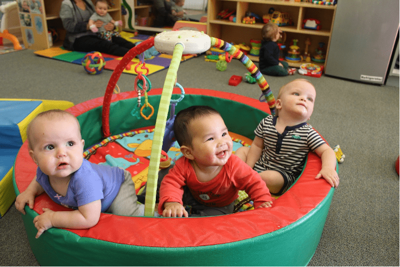 Three babies in activity gym smiling